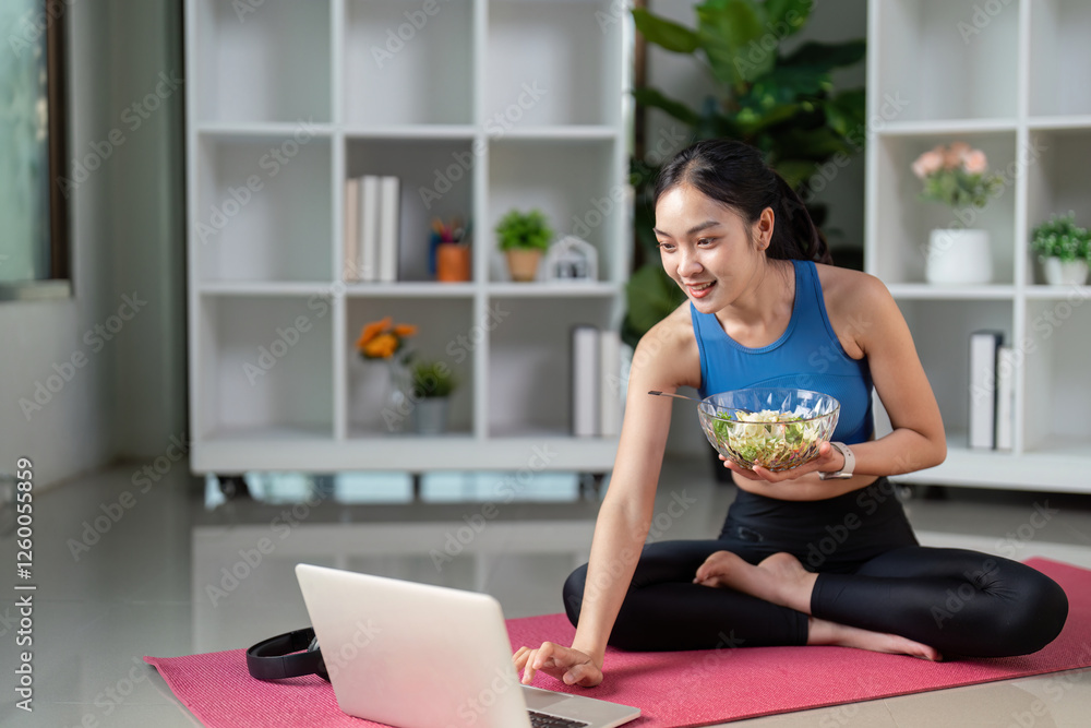 Engaged woman interacting with a laptop while enjoying a salad, combining technology and healthy living.