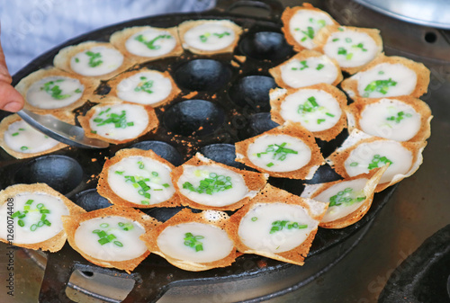 vendor taking Kanom Krok, popular Thai coconut milk pancake out from the pan when ready to serve photo