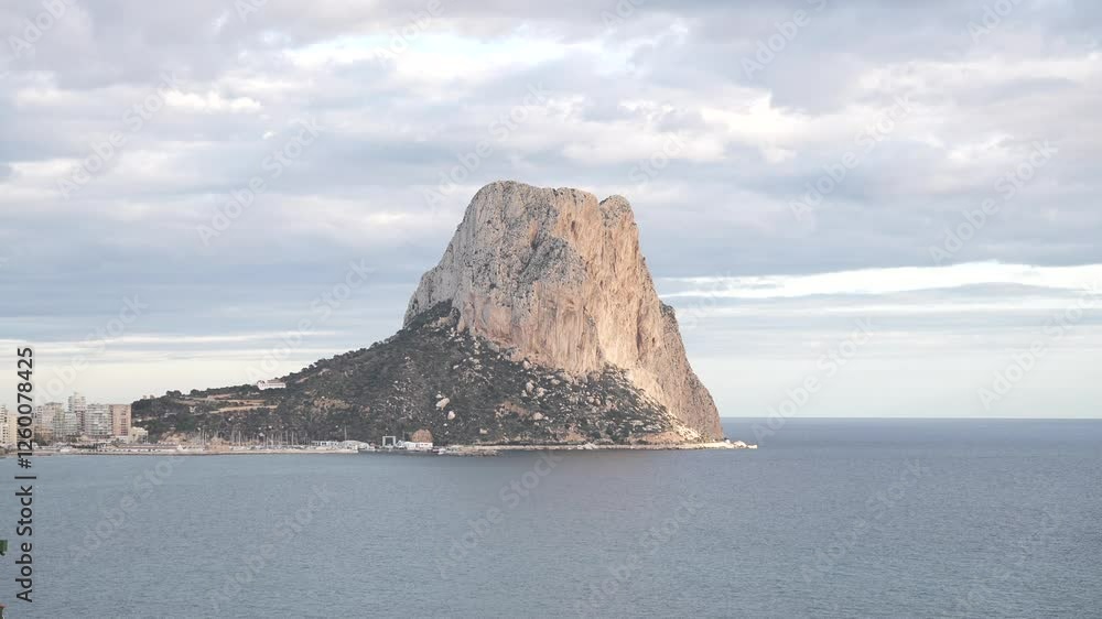 Ifach is in the background of a beautiful ocean view. The sky is cloudy and the water is calm Ifach is in the background of a beautiful ocean view. The sky is cloudy and the water is calm