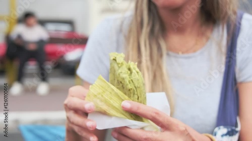 Close-up of young hispanic woman eating street food green tamale, Peruvian street food.