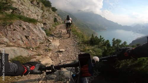 The Barbellino MTB Trail winds along with a reflective alpine lake, combining the excitement of mountain biking with serene natural beauty.