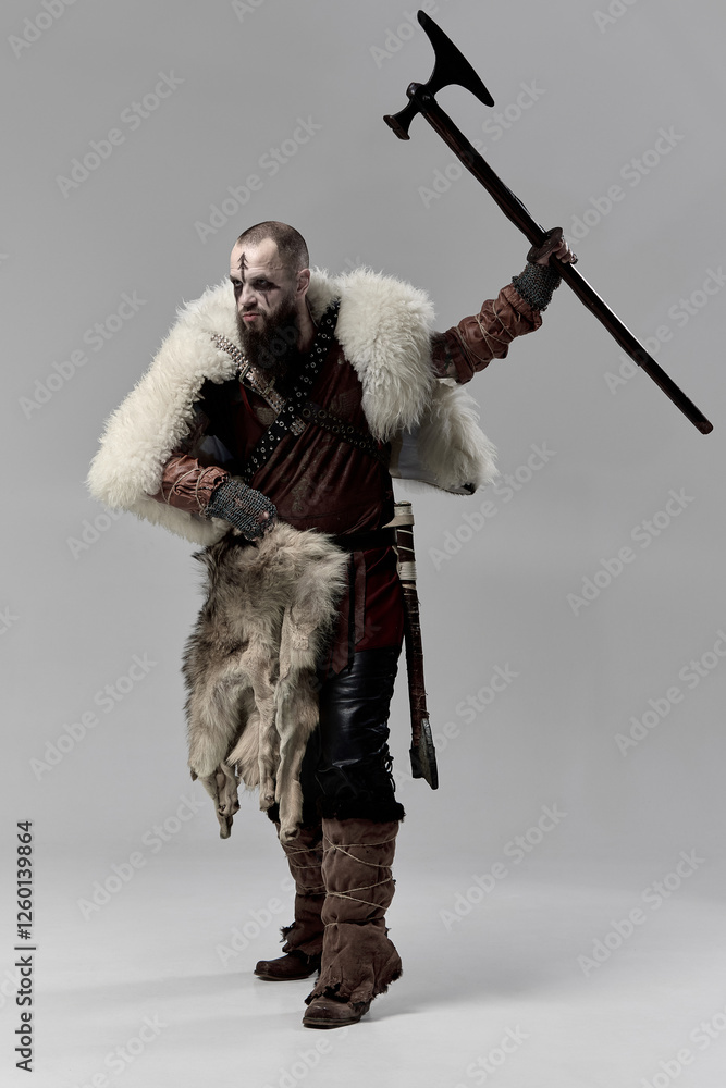 Obraz premium Viking warrior dressed in fur cloak and leather armor, raising battle axe with fierce expression, prepared for combat. Concept of Nordic warrior, medieval history, Norse mythology. Full-length