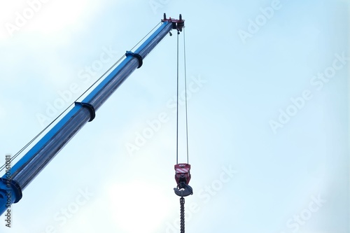 Blue crane arm, boom with hanging hook against clear sky. Construction and lifting heavy building materials, large components, and machinery photo