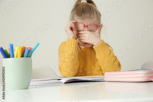 Wallpaper Mural Tired elementary school girl with eyeglasses rubbing her eyes while doing homework Torontodigital.ca