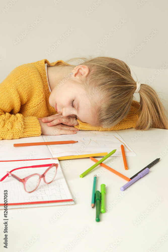 Exhausted elementary school girl is tired of doing homework, sleeping at the kitchen table. Exhausted elementary school girl is tired of doing homework, sleeping at the kitchen table.