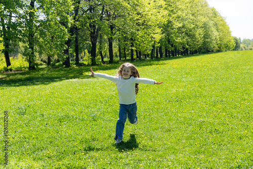 Little girl running across a green meadow in the park from afar towards the camera sunny day with outstretched arms. Freedom concept. Spring time and sunny day. Copy space photo