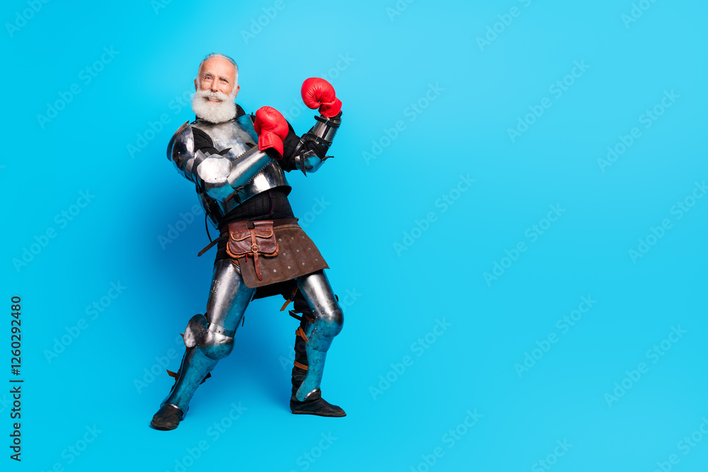 Naklejka premium Elderly man dressed as a knight with boxing gloves posing against a bright blue background in a medieval costume and modern additions
