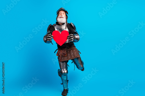 Smiling knight in steel armor holding a heart symbol over a blue background for a love and medieval concept photo