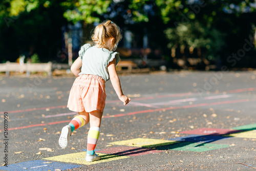 Foto Cute little toddler girl playing hopscotch game drawn with colorful chalks on asphalt