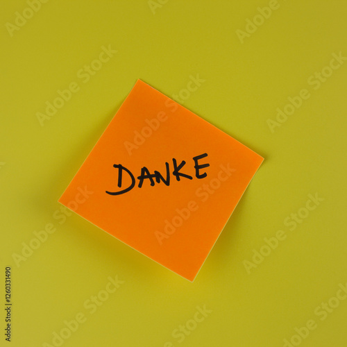 Danke, thank you in german, written in black capital letters on an orange sticky note against a yellow background