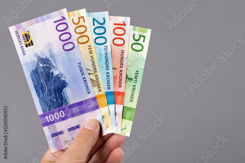 Norwegian krone in the hand on a gray background