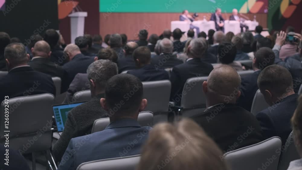 Large audience gathered in a conference room attending a formal seminar or business talk. Large audience gathered in a conference room attending a formal seminar or business talk.