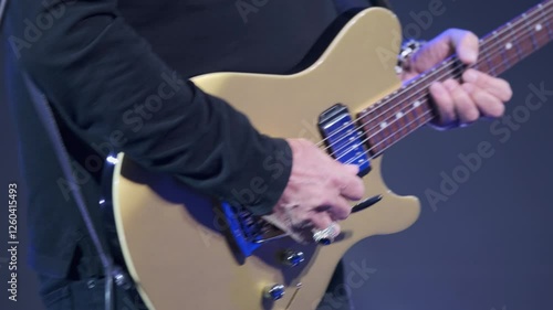Close-up of a musician playing a gold electric guitar, showcasing their hands and the instrument during a live music performance. Suitable for themes of music, performance, and instrumental artistry.