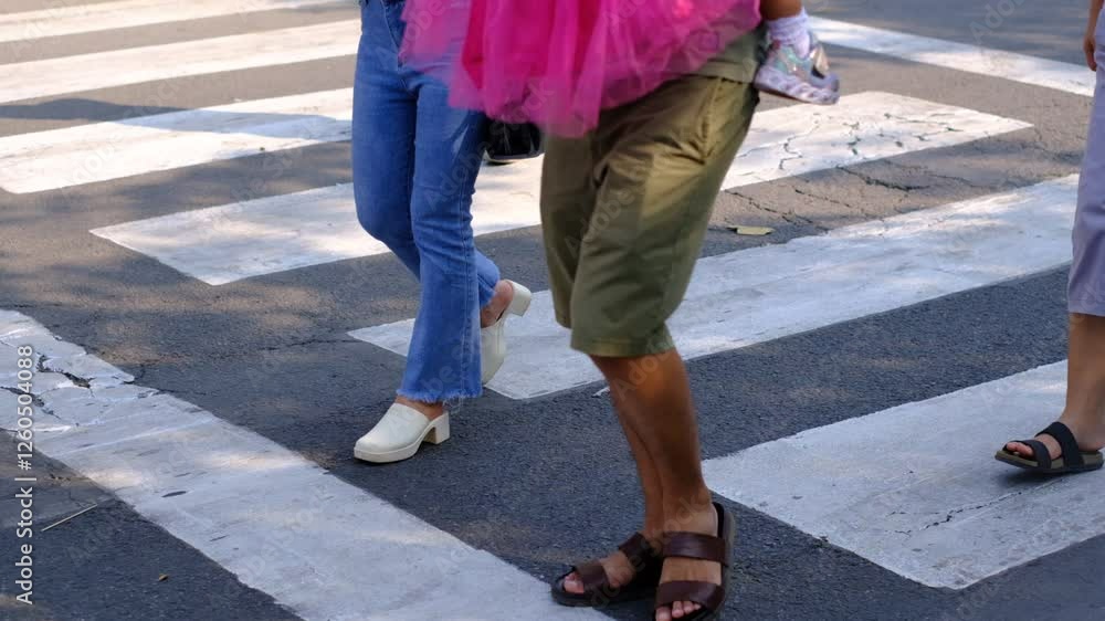 A woman is crossing a street with a man in a green shirt behind her. The woman is wearing blue jeans and white shoes A woman is crossing a street with a man in a green shirt behind her. The woman is wearing blue jeans and white shoes