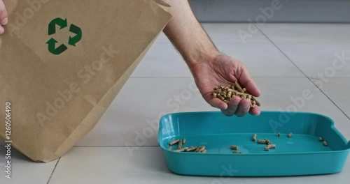 Man gently pours pellets from hand into cat litter box. Person pulls hand full of filler from paper bag over sipping into pet litter tray