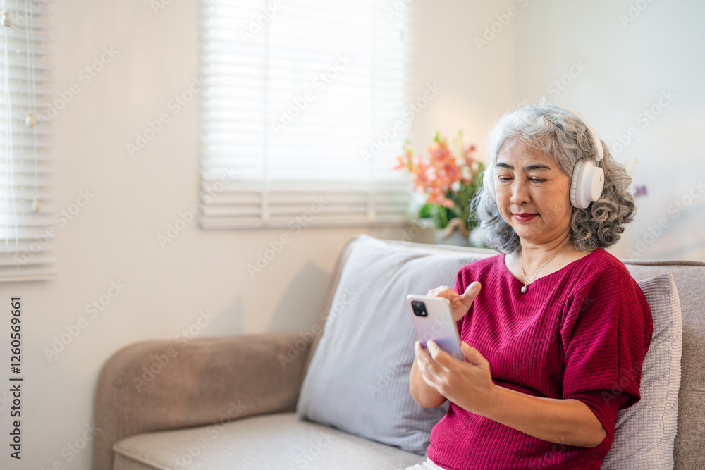 One mature gray haired woman with headphones at home listen music online happy smile hold mobile phone smartphone use app application sit on the sofa bed One mature gray haired woman with headphones at home listen music online happy smile hold mobile phone smartphone use app application sit on the sofa bed