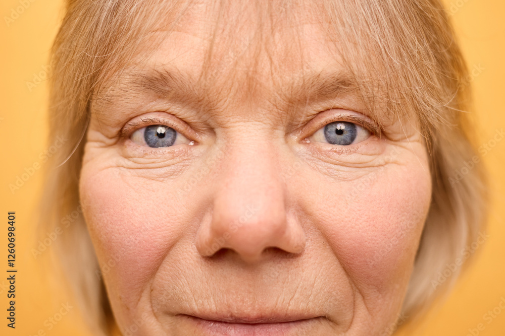 Close-up of a woman with light blonde hair and captivating blue eyes. Her expression reveals warmth and confidence, with a bright yellow background enhancing the visual impact Close-up of a woman with light blonde hair and captivating blue eyes. Her expression reveals warmth and confidence, with a bright yellow background enhancing the visual impact
