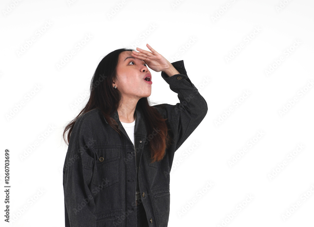 Amazed asian woman wearing black denim jacket looking at something far away with hand on forehead gesture isolated on horizontal white background. Amazed asian woman wearing black denim jacket looking at something far away with hand on forehead gesture isolated on horizontal white background.