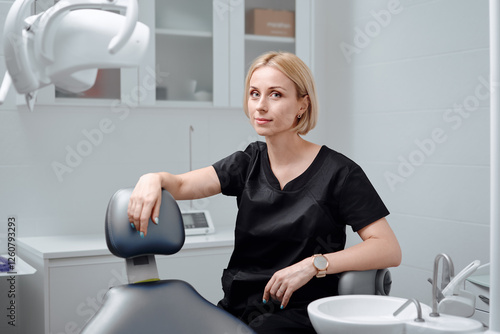 Young blonde woman dentist posing at modern dental cabinet next to dental chair. Pretty stomatologist at dental clinic