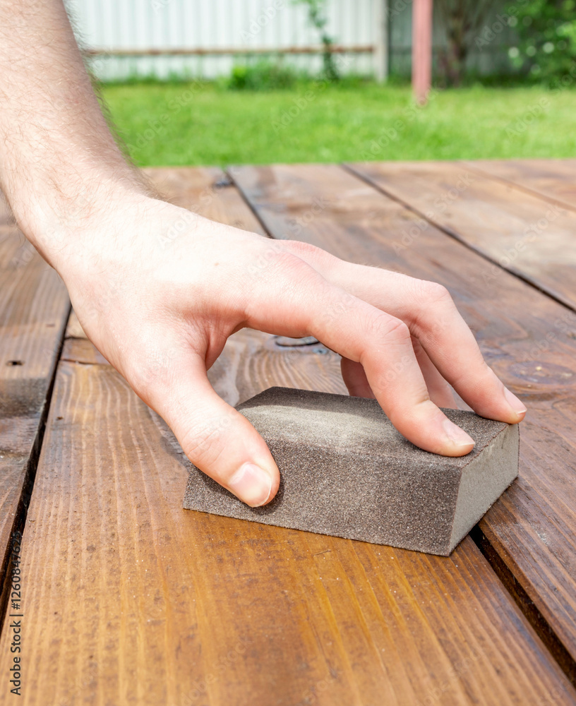 Hand is holding a sanding block on a wooden surface