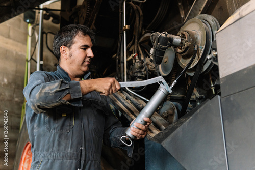 Farmer greasing combine harvester with grease gun during maintenance in garage