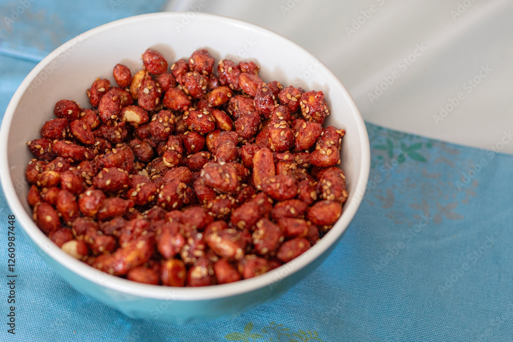 Candied peanuts in a white bowl on table with blue placemats and white tablecloth. Snack ready to serve Candied peanuts in a white bowl on table with blue placemats and white tablecloth. Snack ready to serve