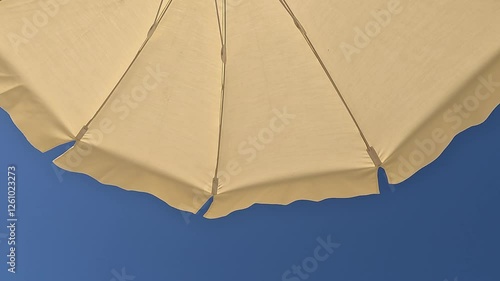 White beach umbrella. Blue sky in the background. View from below. Relaxing context. Summer holidays by the sea. General contest and location