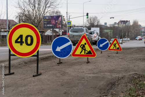 Brightly colored traffic signs indicate a speed limit and direct drivers among ongoing road work in a city environment photo