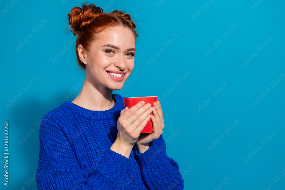 Smiling young woman holding red mug against vibrant blue background, dressed in casual knitted sweater showcasing cozy winter style Smiling young woman holding red mug against vibrant blue background, dressed in casual knitted sweater showcasing cozy winter style