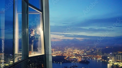 Mid adult businesswoman standing in a corporate windows with view of the city, talking on her mobile phone
