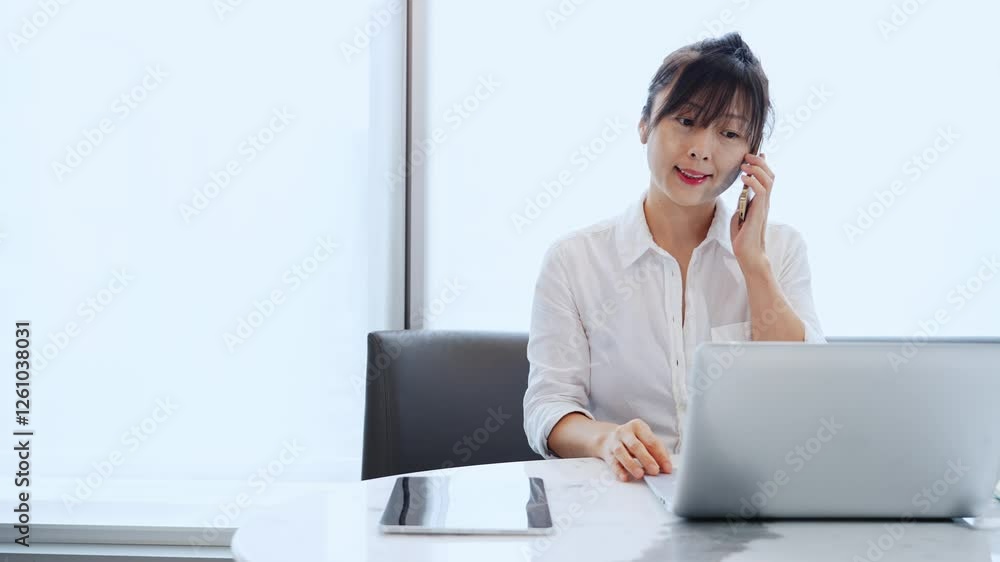 Young businesswoman with digital tablet and laptop talking on mobile phone at desk in office, slow motion video Young businesswoman with digital tablet and laptop talking on mobile phone at desk in office, slow motion video