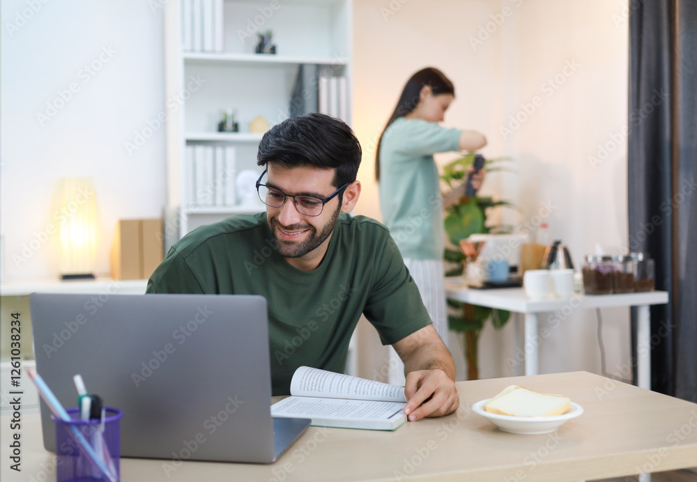 Image of a handsome white man looking at a laptop and working online from home with his girlfriend making him coffee. Image of a handsome white man looking at a laptop and working online from home with his girlfriend making him coffee.