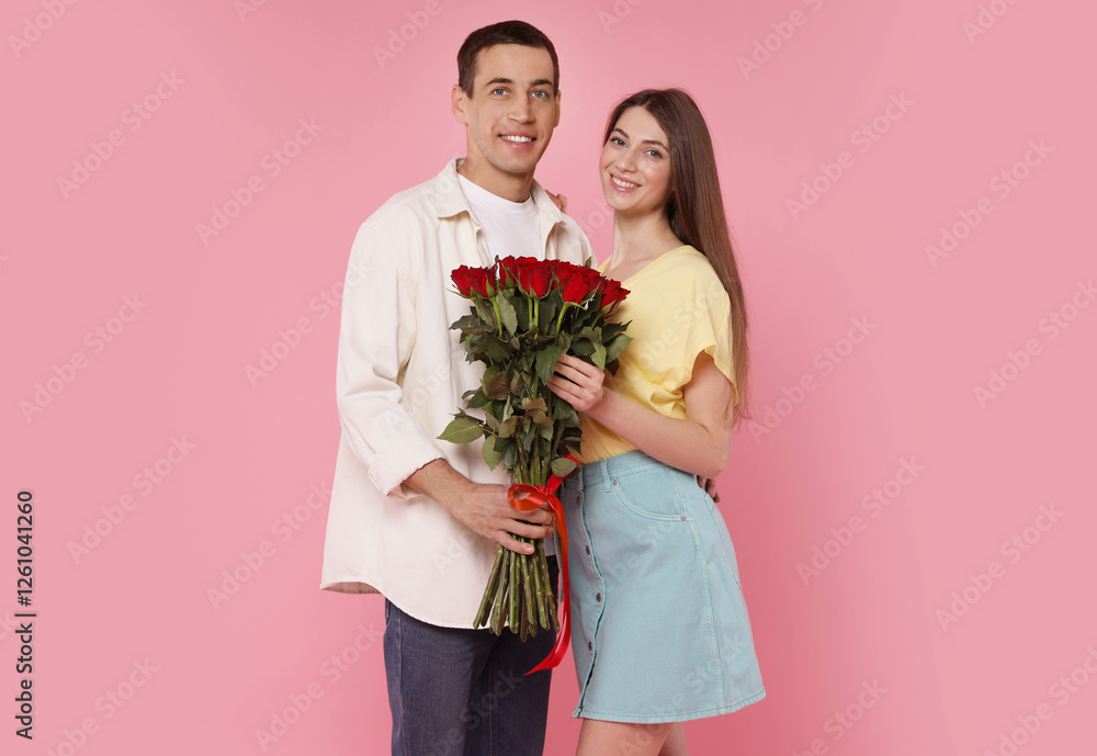 Lovely couple with bouquet of red roses on pink background. Valentine's day celebration Lovely couple with bouquet of red roses on pink background. Valentine's day celebration