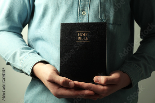 Man with hardcover Holy Bible on light background, closeup photo