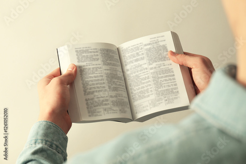 Man reading Holy Bible in English language on light background, closeup photo