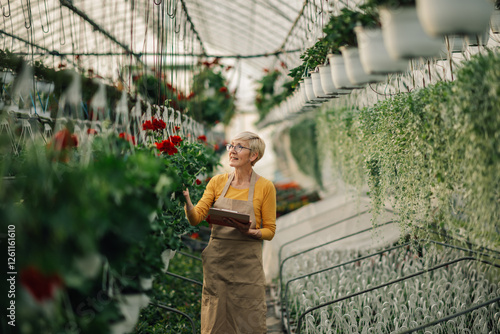 Happy old florist with clipboard at hothouse checking on vertical garden