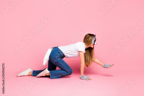 Young woman in casual outfit posing playfully on all fours with animal costume elements against pastel pink background photo