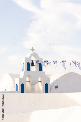 Blue and white traditional church on Santorini, Greece, with Greek flags hanging in the breeze on a clear day.