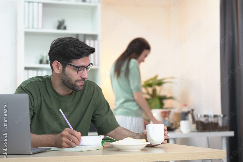 Young professional freelancing at home, texting on a phone in a stylish, well-lit living room. A woman enjoying on the sofa in the background Young professional freelancing at home, texting on a phone in a stylish, well-lit living room. A woman enjoying on the sofa in the background