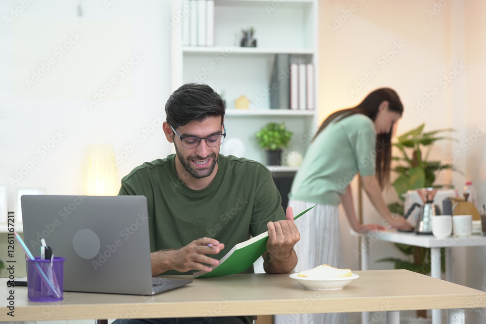 Young professional freelancing at home, texting on a phone in a stylish, well-lit living room. A woman enjoying on the sofa in the background Young professional freelancing at home, texting on a phone in a stylish, well-lit living room. A woman enjoying on the sofa in the background