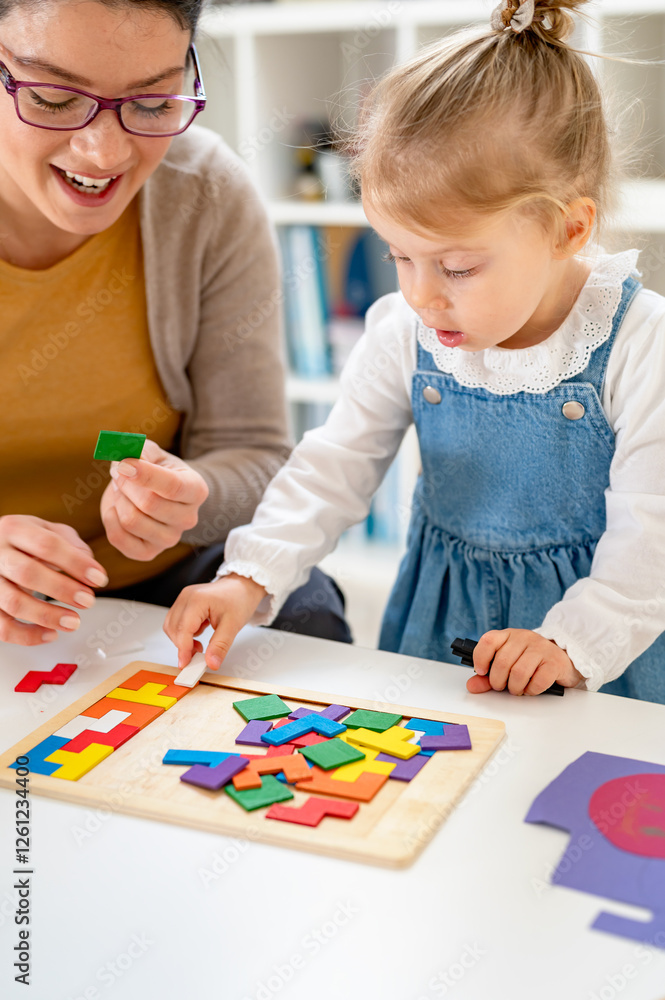 A caring teacher and a toddler girl engage in a hands-on learning activity with colorful wooden puzzles in a bright and organized classroom A caring teacher and a toddler girl engage in a hands-on learning activity with colorful wooden puzzles in a bright and organized classroom