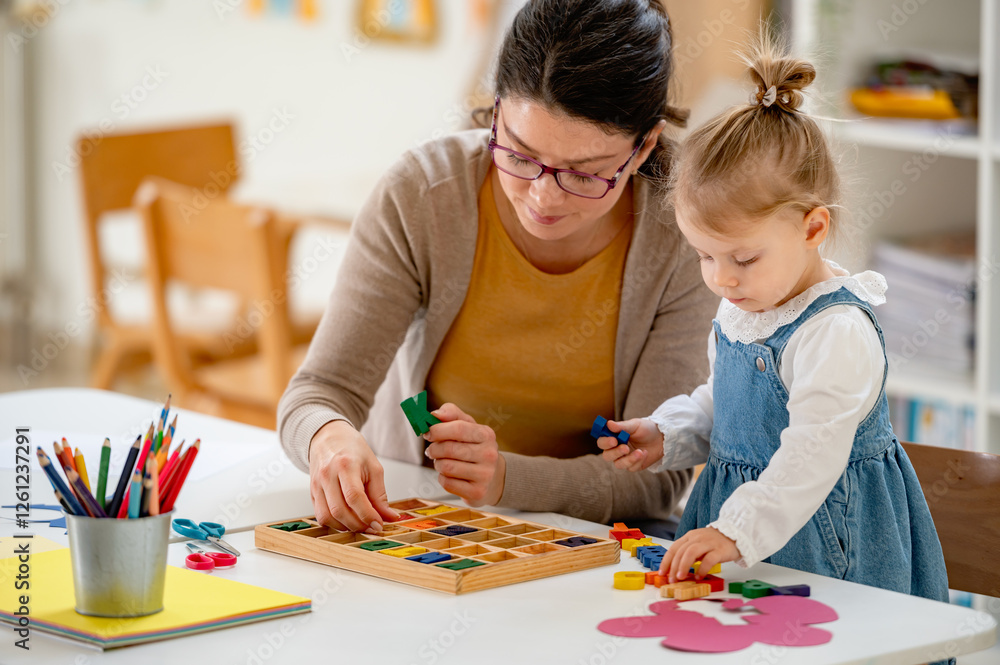 Fototapeta premium A caring teacher and a toddler girl play with wooden letters, exploring language and early literacy skills in a bright and engaging classroom