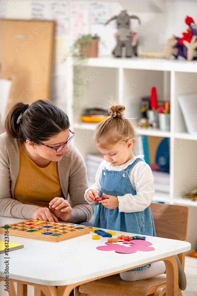 A caring teacher and a toddler girl engage in a hands-on learning activity with colorful wooden puzzles in a bright and organized classroom A caring teacher and a toddler girl engage in a hands-on learning activity with colorful wooden puzzles in a bright and organized classroom