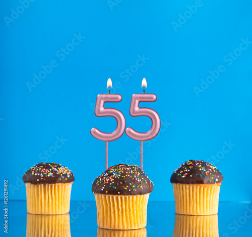 Birthday candle with the number 55 - Three cupcakes on a blue background. photo