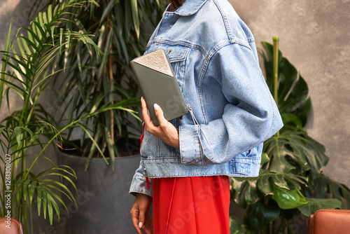 Obraz na płótnie Fashionable woman in denim jacket holding stylish diary in urban greenery setting, modern lifestyle concept w salonie