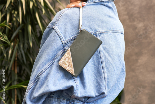 Stylish faux leather clutch with elegant pattern design resting on denim jacket sleeve fashion accessory concept photo