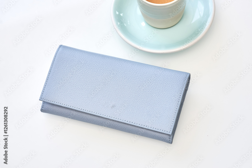 Stylish blue wallet resting near elegant espresso cup on white background, minimalist luxury fashion concept