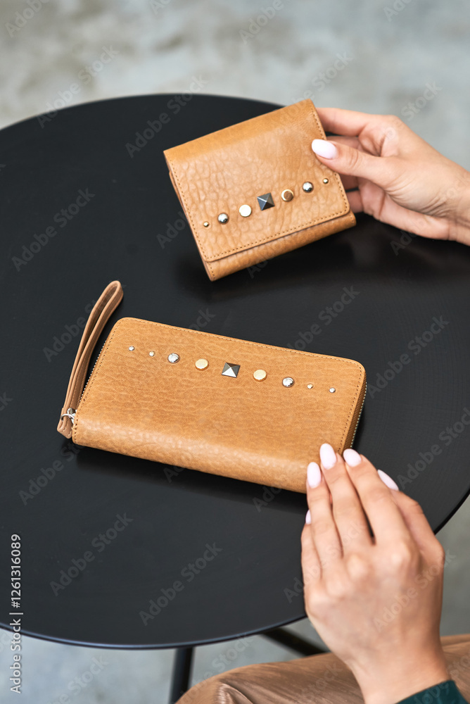 Elegant brown leather wallet and purse with studs in hands on dark table, fashion accessory concept