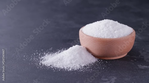 salt in a wooden bowl on a black stone table. Salt spilling on a black stone table .