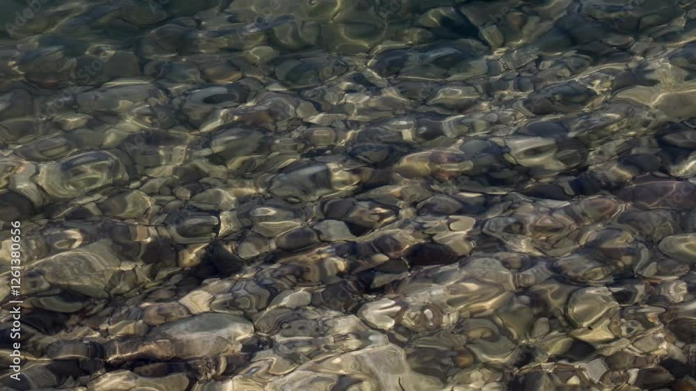 Clear water over smooth pebbles at Lake Garda, Sirmione, Italy, reflecting sunlight with natural pattern